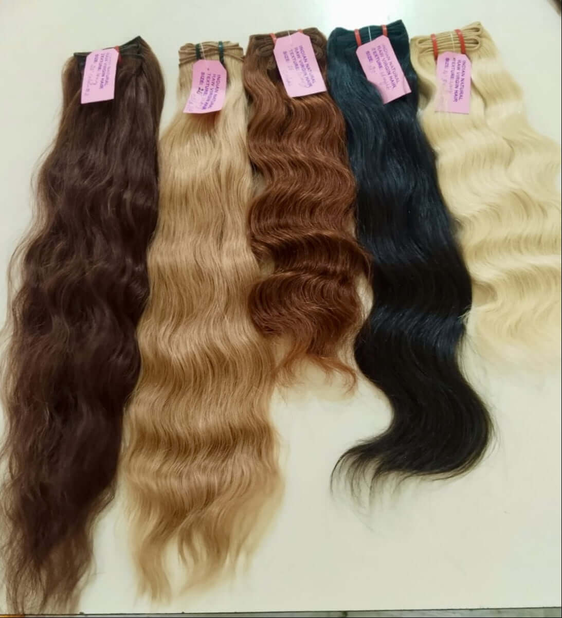 Five bundles of wavy hair extensions in different colors with pink tags on a white background.