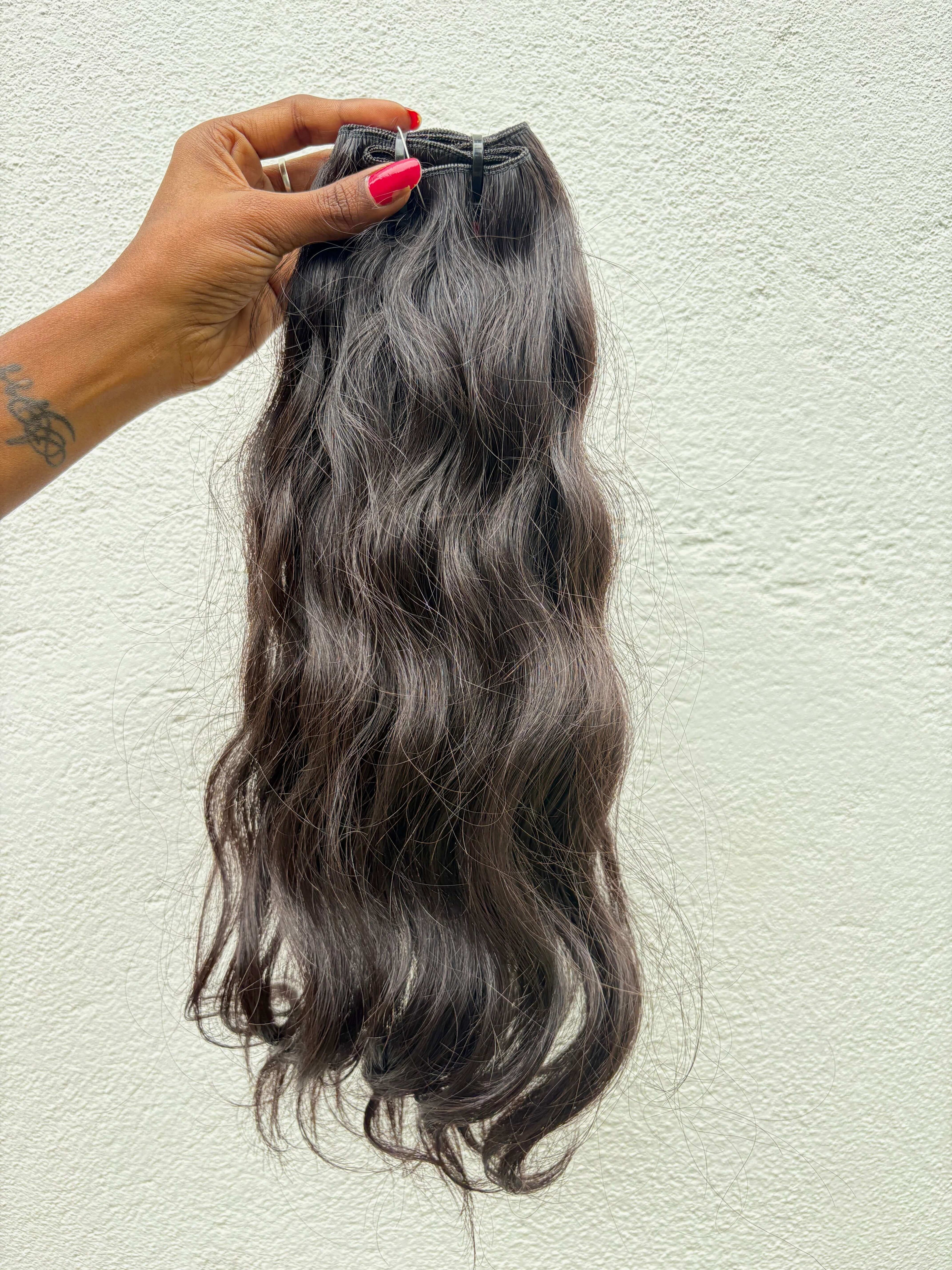 Wavy Raw Indian Hair extensions held by a hand against a light background