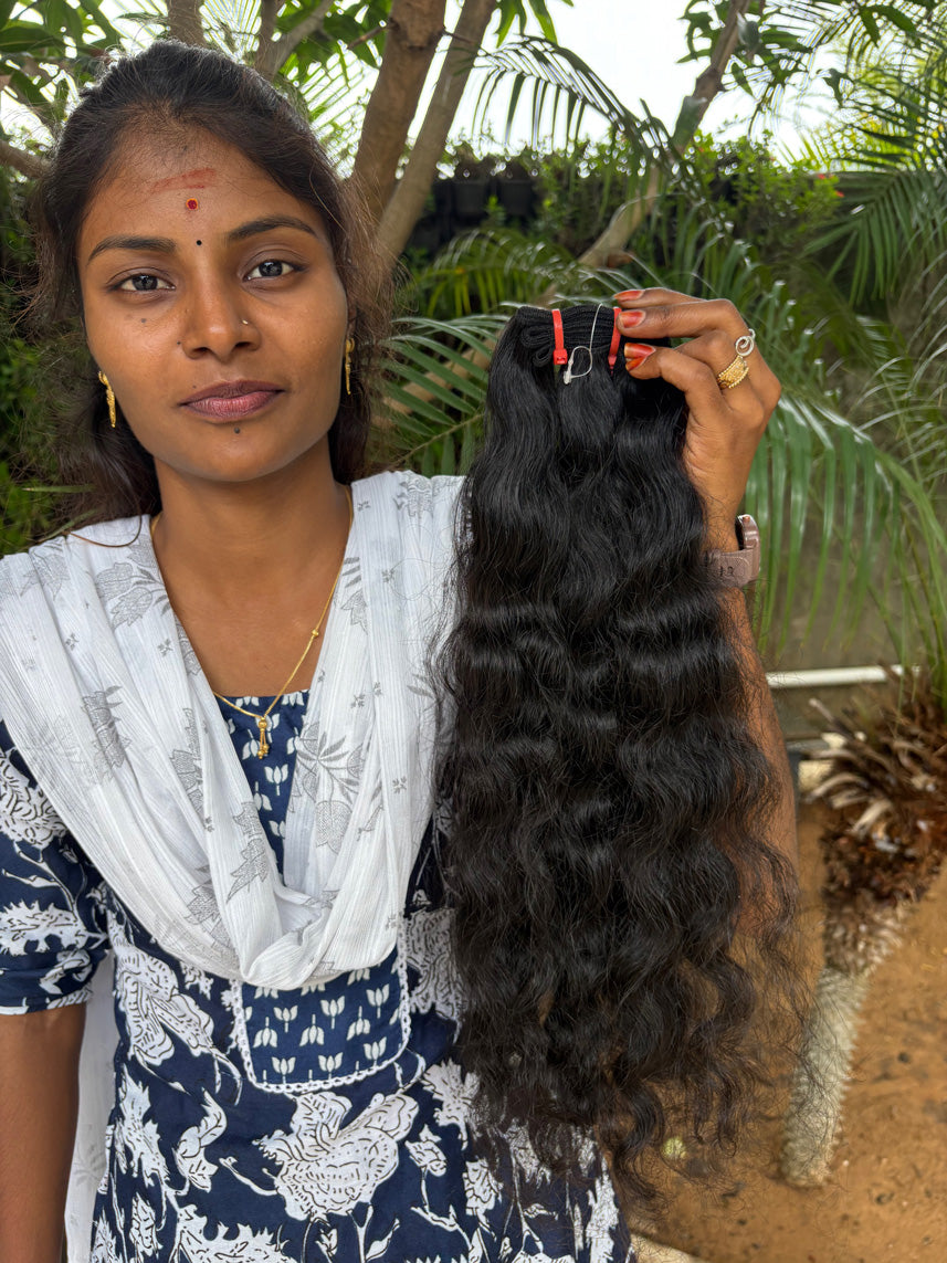 Woman holding a long bundle of natural black wavy raw Indian hair extensions outdoors