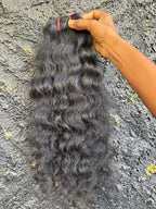 Loose curly Raw Indian Hair bundles against a black wall.