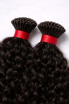 Professional installation of curly keratin I-tip extensions, demonstrating a seamless, undetectable blend for added length and voluminous curls.