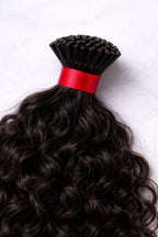 Macro view of the natural curly pattern of raw Indian I-tip extensions, showcasing the healthy luster and cuticle-aligned strength of temple-sourced hair.