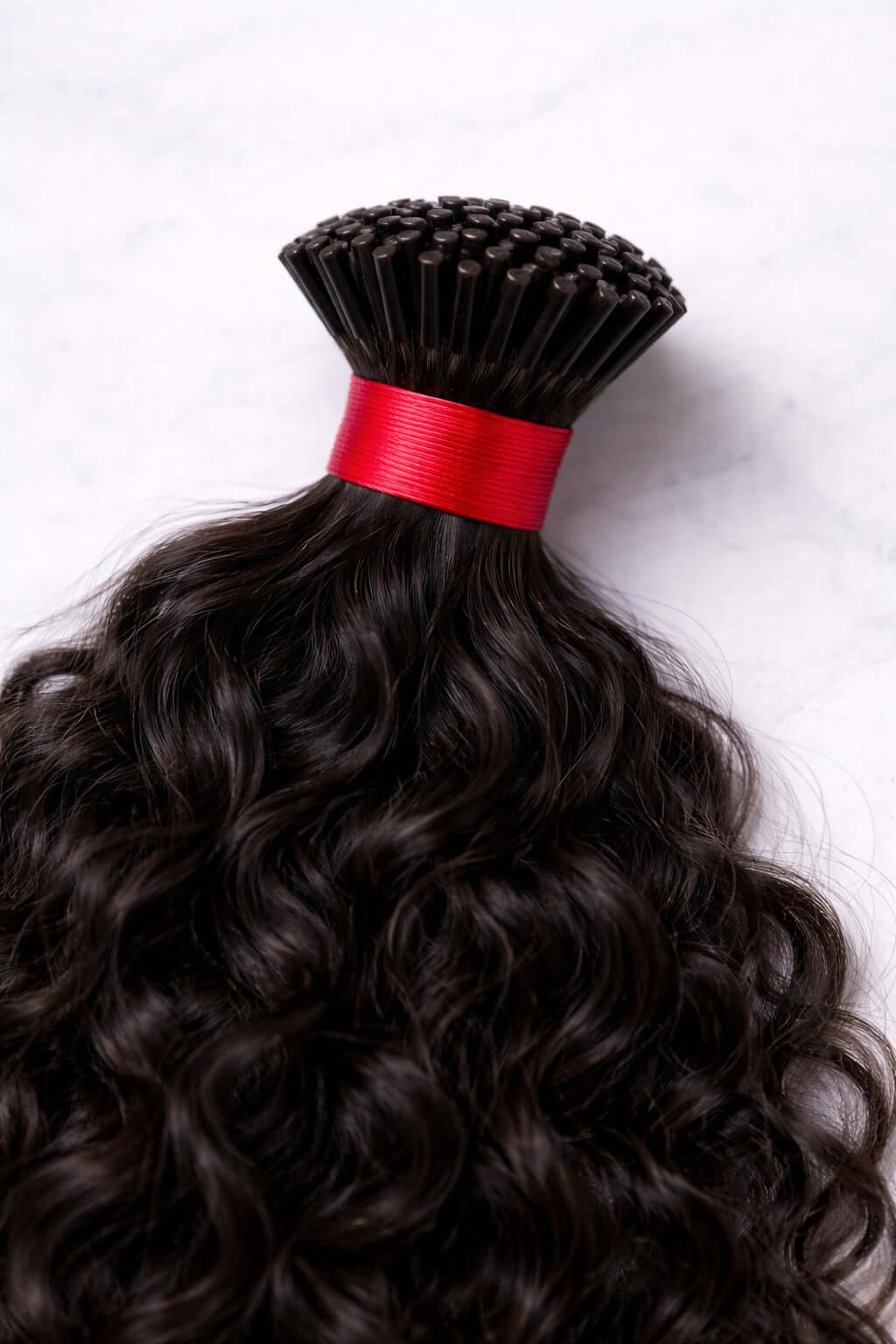 Macro view of the natural curly pattern of raw Indian I-tip extensions, showcasing the healthy luster and cuticle-aligned strength of temple-sourced hair.